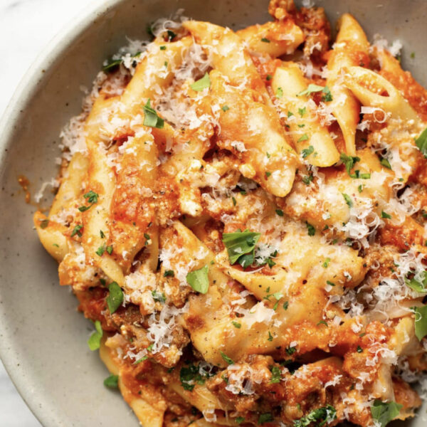 A bowl of pasta with tomato meat sauce, topped with grated cheese and fresh herbs.