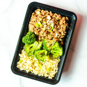 A black meal container with cooked ground beef topped with chopped green onions, steamed broccoli, and a serving of brown rice.