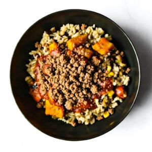 The F*d Up Fajita: A black bowl filled with spiral pasta, corn, tomato sauce, squash chunks, and crumbled ground meat on top.