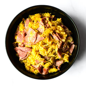 A black bowl of The F*d Up Fajita, featuring rotini pasta, shredded meat, and creamy yellow sauce, viewed from above.