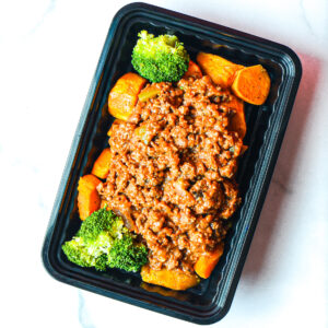 A black meal tray with ground meat in sauce over roasted sweet potatoes, served with broccoli florets on each side.