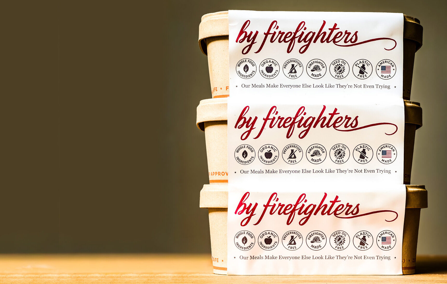 Three stacked food containers labeled by firefighters with icons and text claiming their meals make everyone else look like theyre not even trying.