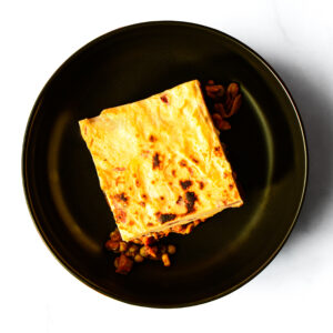 A serving of The F*d Up Fajita is presented on a black plate, with its filling visible around the edges, set against a white background.