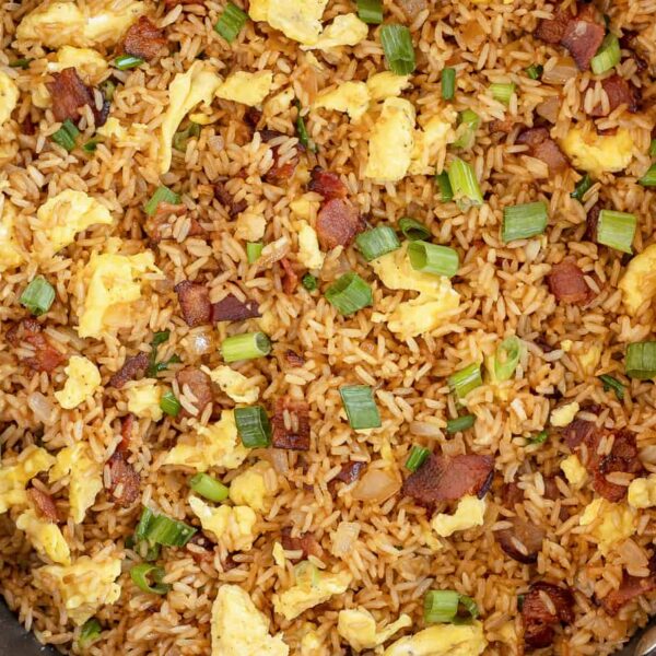 A skillet of Good Morning, Dumbass!—fried rice, scrambled eggs, bacon, and green onions—sits on marble beside a striped towel and a bowl of green onions.