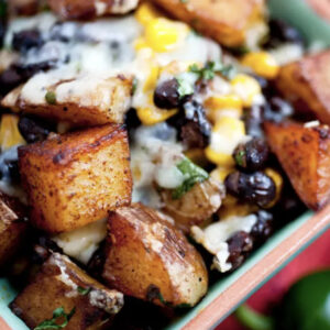 Close-up of roasted potato cubes topped with melted cheese, black beans, corn, and chopped herbs in a bowl.