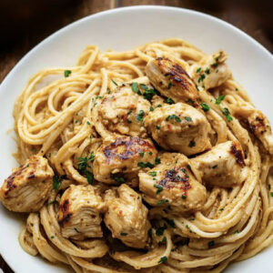 A white bowl filled with High Noon Linguine, topped with grilled chicken pieces and sprinkled with chopped herbs.