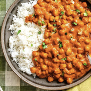Code Red Chickpeas in a creamy orange curry sauce served over white rice, garnished with chopped herbs.