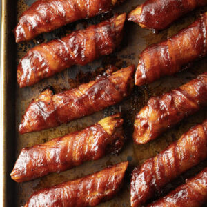 Do I Make You Meaty? Do I?! bacon-wrapped breadsticks glazed with barbecue sauce are placed on a baking sheet.