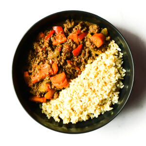 A black bowl filled with ground beef and red bell peppers on one side, and cooked rice on the other side, viewed from above.