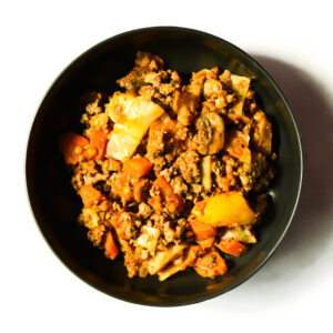 A black bowl filled with a mixture of ground beef, chopped vegetables, and sauce, photographed from above on a white background.