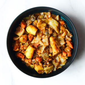 A bowl of vegetable stew with potatoes, carrots, cabbage, and other assorted vegetables in a tomato-based sauce.