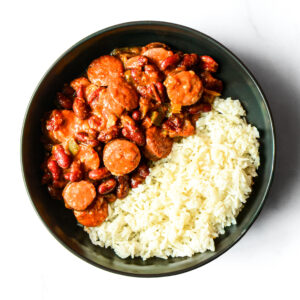 A bowl containing white rice on one side and red beans with sausage in a tomato-based sauce on the other side.