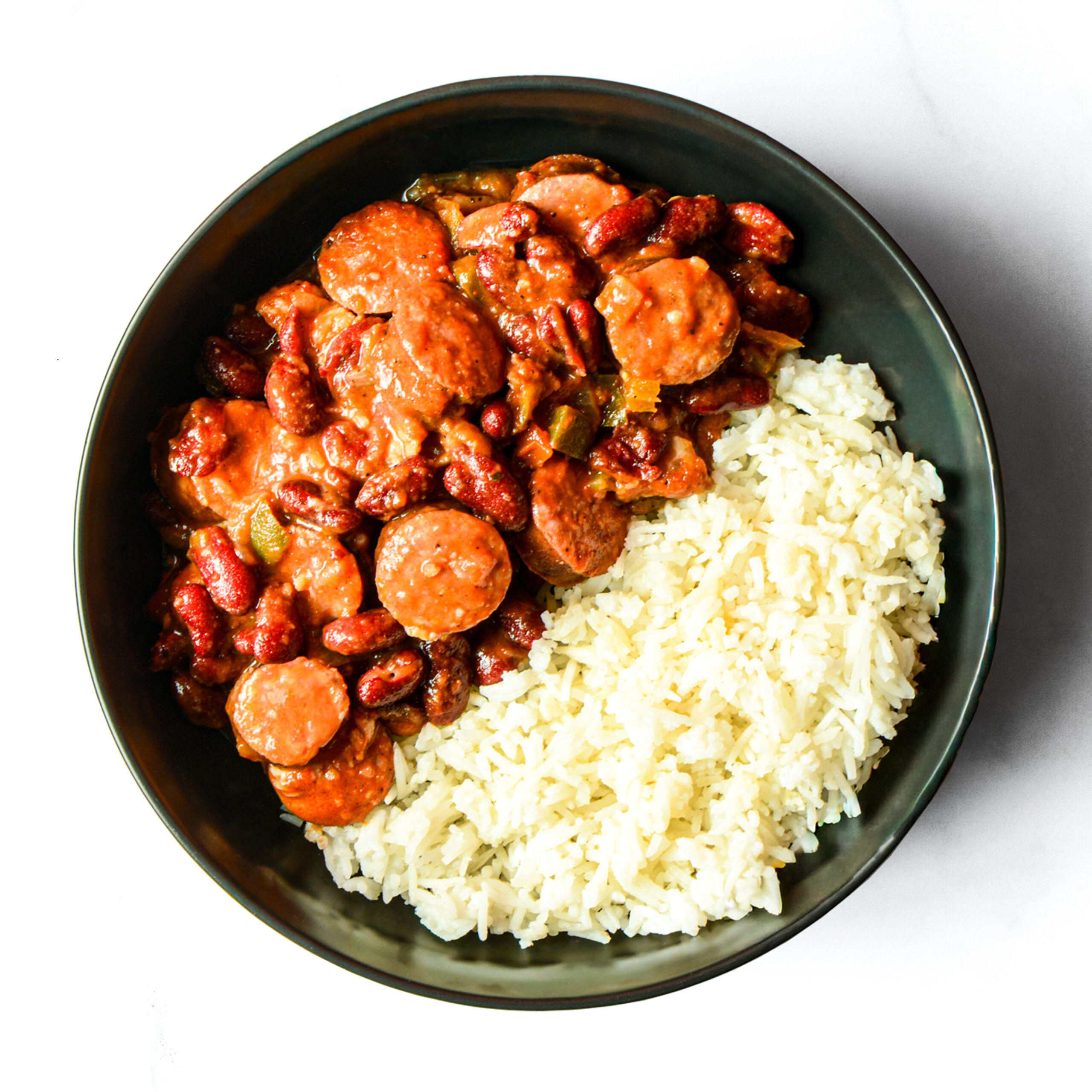A bowl containing white rice on one side and red beans with sausage in a tomato-based sauce on the other side.