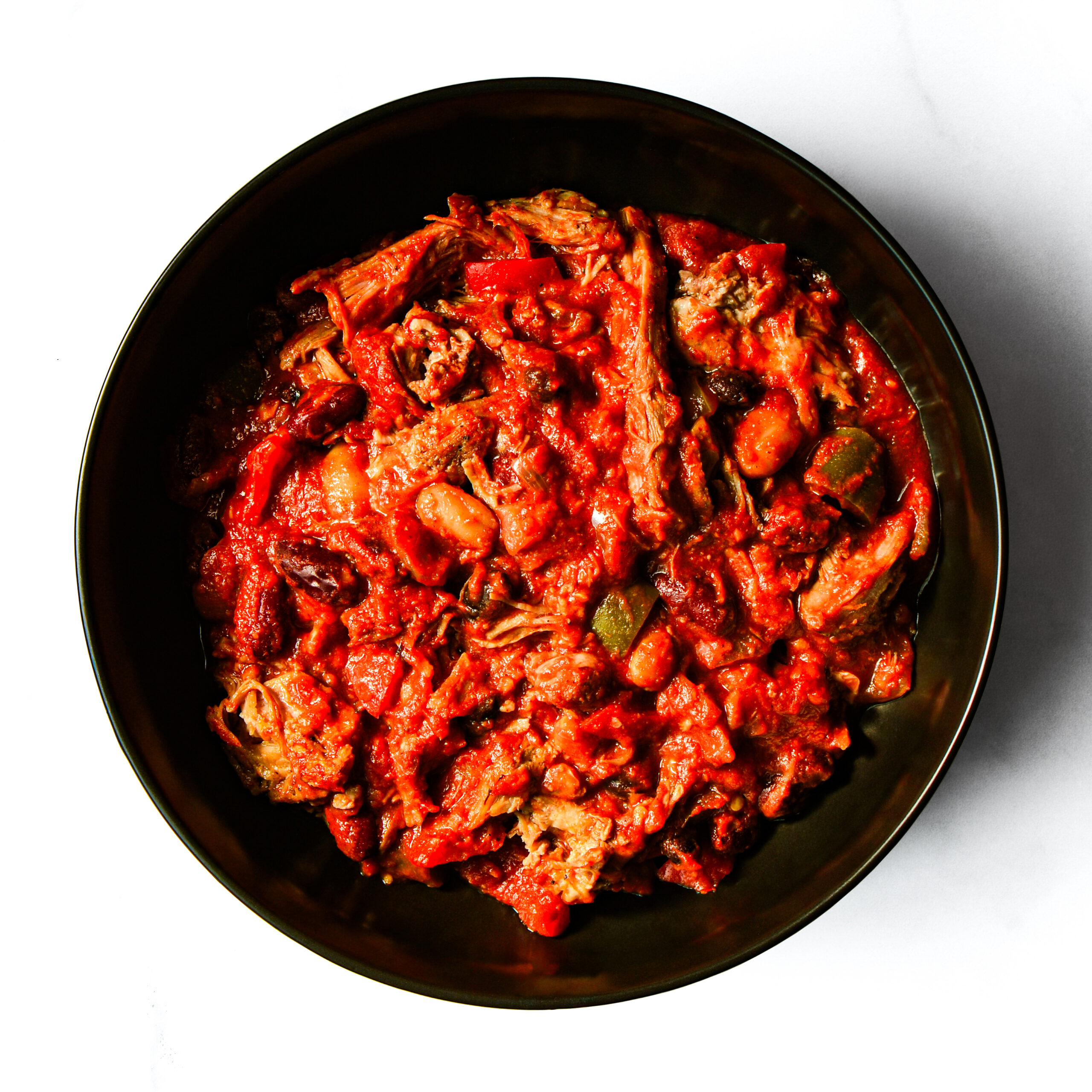A bowl filled with shredded meat in a red tomato-based sauce with visible pieces of vegetables.