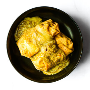 A folded omelette covered in melted cheese and sauce, served on a black plate against a white background.