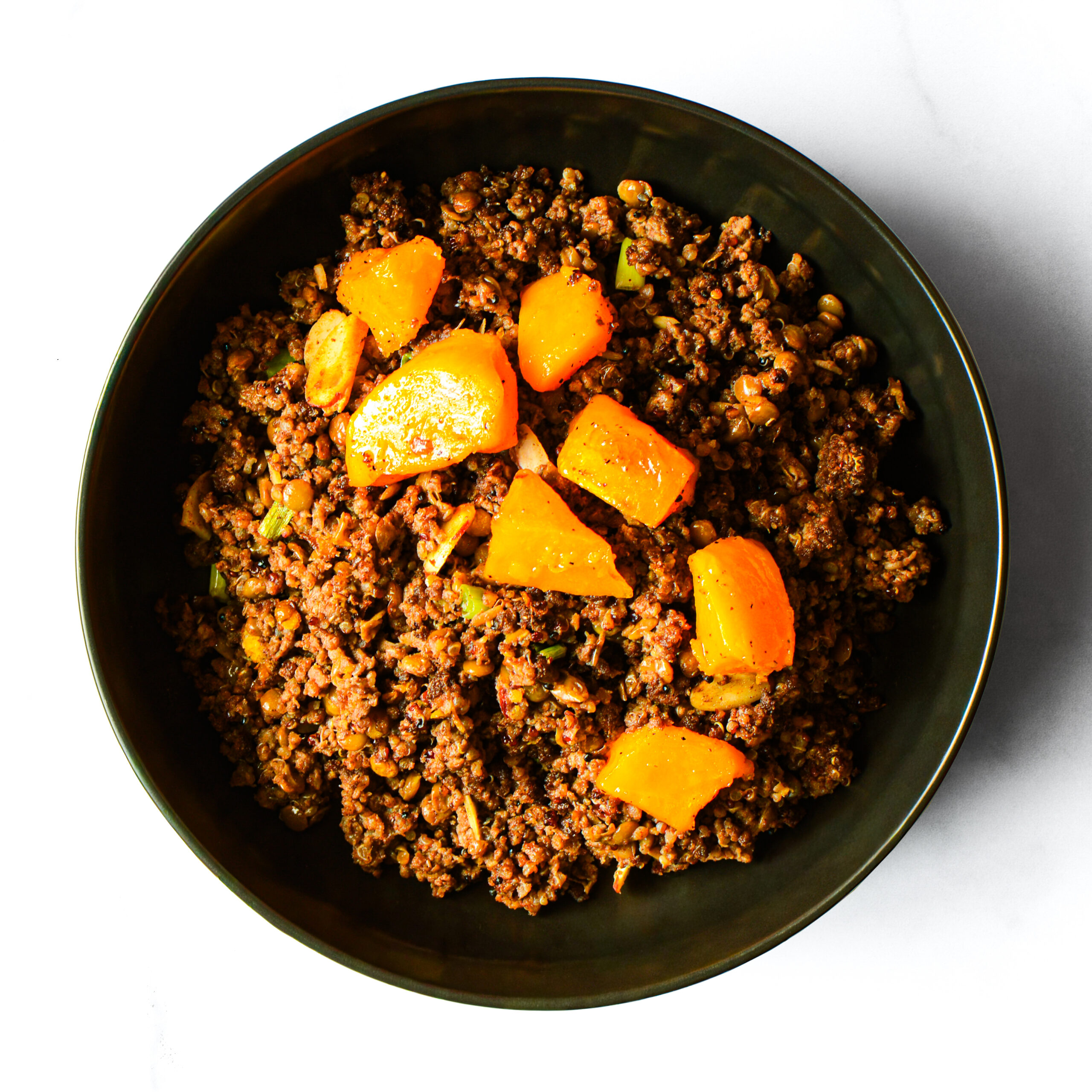 A black bowl filled with ground beef, diced cooked potatoes, and chopped vegetables on a white surface.