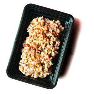 A black plastic container filled with a creamy, chunky mixture containing visible pecans.