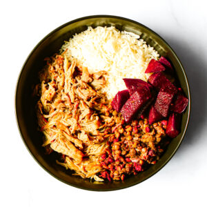 A bowl containing white rice, shredded chicken, cooked lentils with vegetables, and sliced cooked beets, arranged in separate sections.