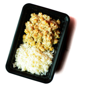 A black plastic container holding white rice and a serving of creamy chickpea curry.