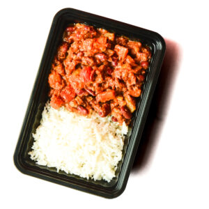 A black tray containing white rice on one side and a red chili with beans and vegetables on the other side.