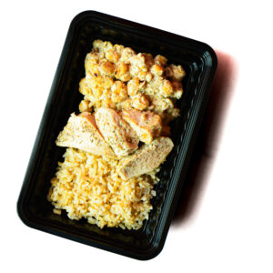 A black plastic meal tray containing yellow rice, sliced chicken breast, and a chickpea mixture.