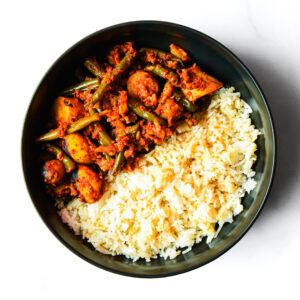A black bowl containing white rice on one side and a vegetable curry with green beans, potatoes, and sauce on the other side.