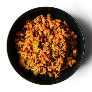 A black bowl filled with a rice dish containing vegetables and beans, photographed from above on a white background.