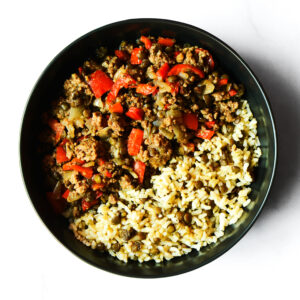 A black bowl filled with cooked ground beef, red bell peppers, onions, rice, and green lentils.