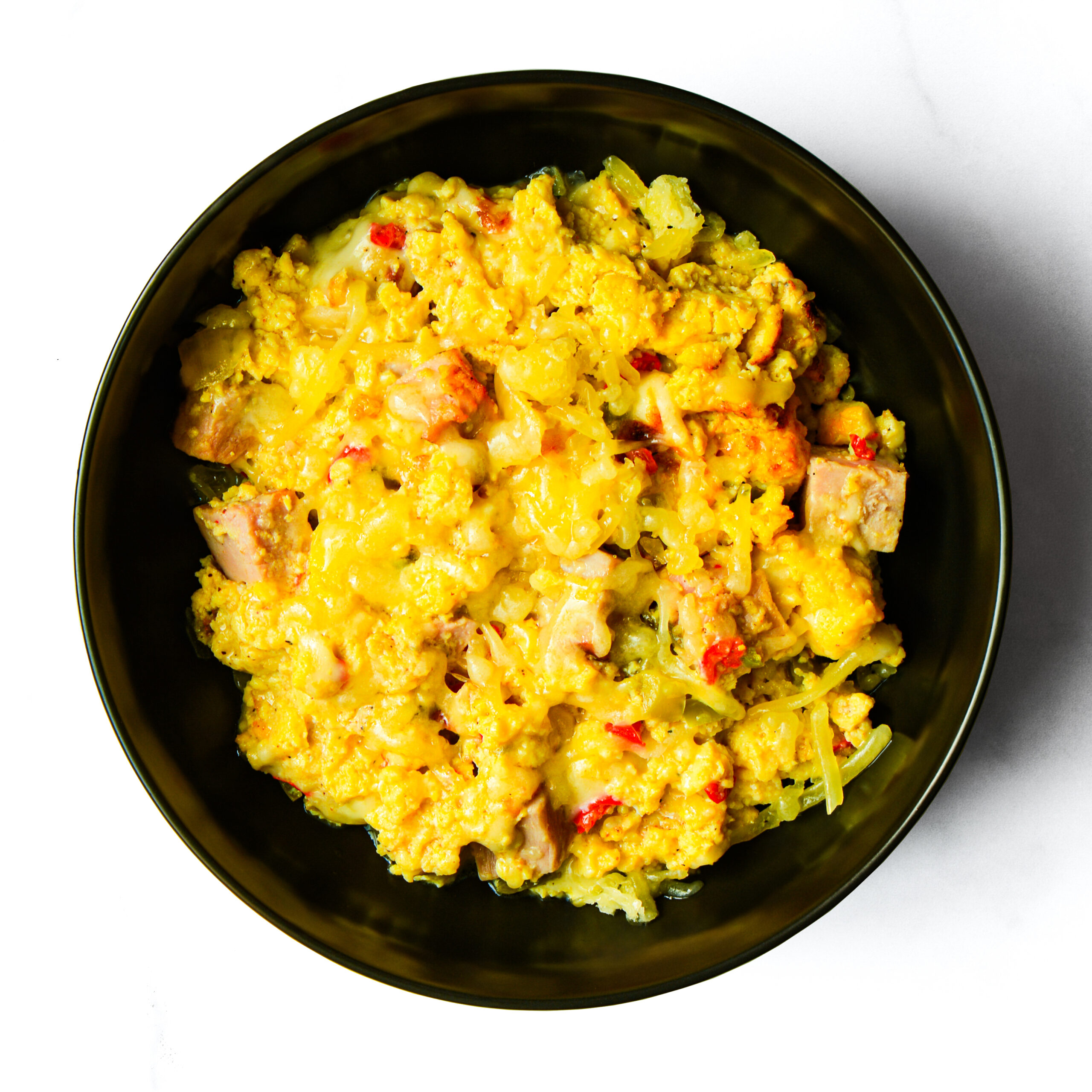 A black bowl filled with a yellow rice dish containing chunks of meat and red pepper pieces, viewed from above.