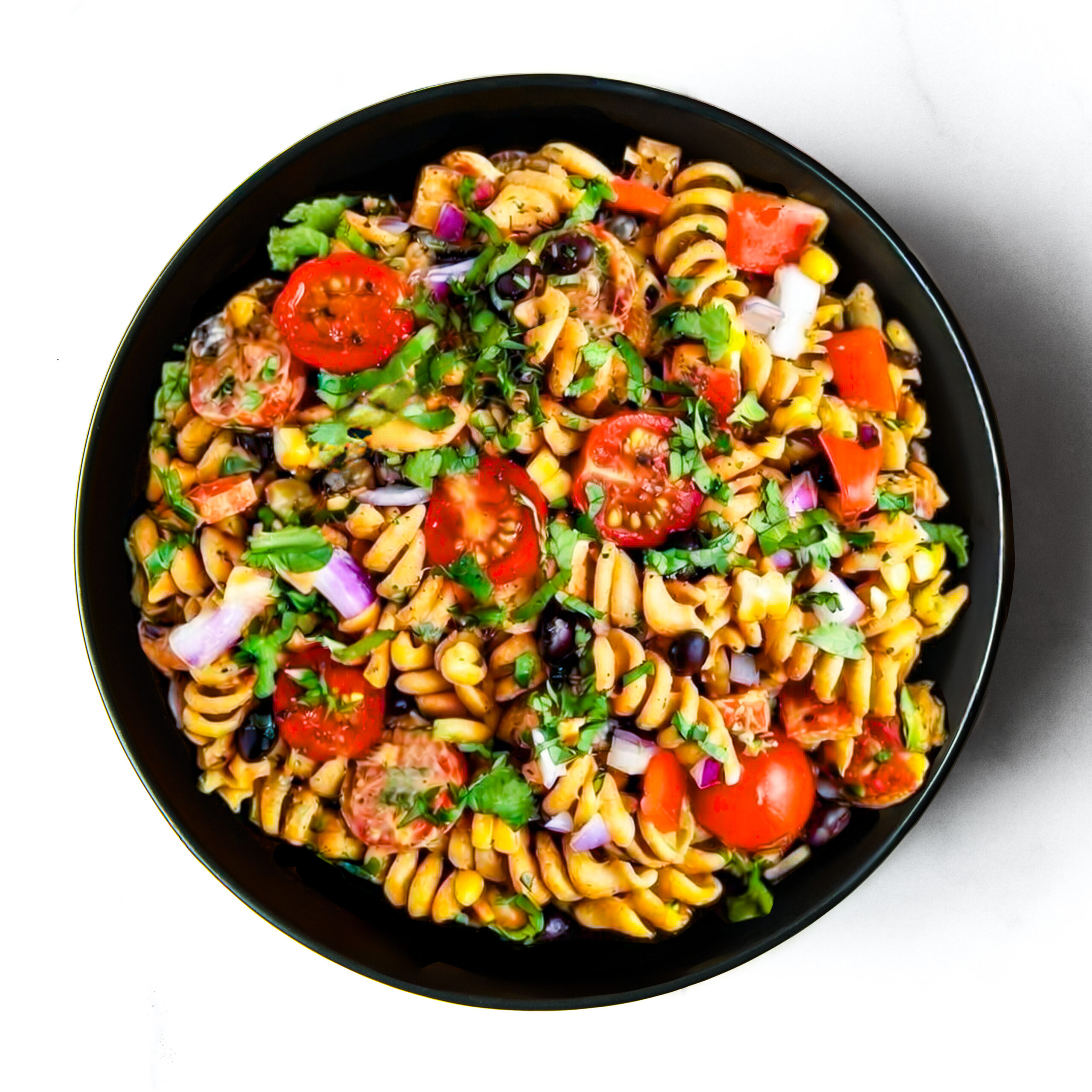 A black bowl filled with rotini pasta salad, cherry tomatoes, red onions, black beans, diced peppers, and cilantro on a white surface.