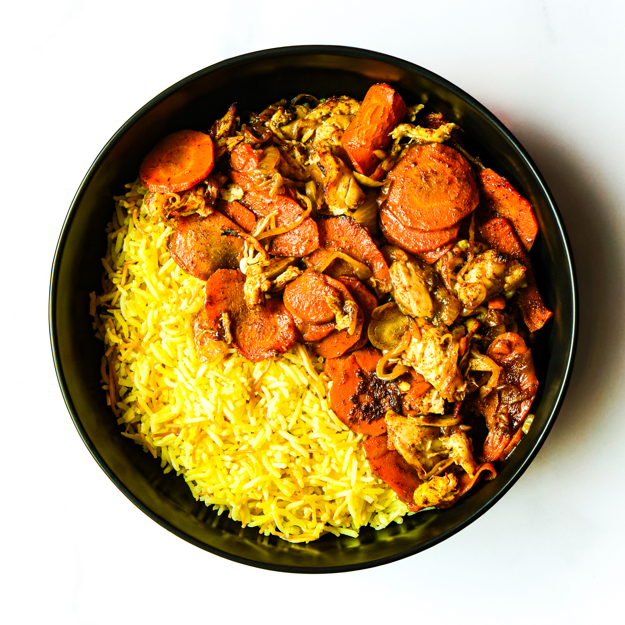 A black bowl filled with yellow rice and a cooked mixture of sliced carrots, chicken, and onions.