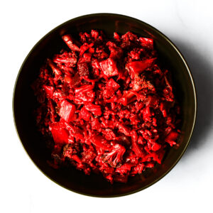 A black bowl filled with bright red chopped vegetables, including pieces resembling broccoli and possibly cabbage, on a white background.