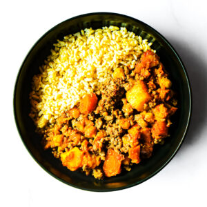 A black bowl filled with yellow rice on one side and a ground meat and vegetable curry on the other, photographed from above on a white background.