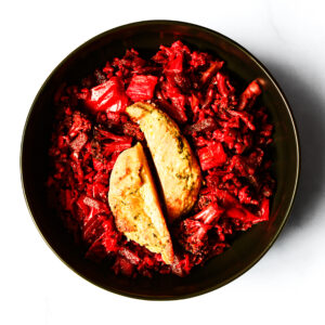 A black bowl filled with shredded red vegetables and topped with two pieces of seasoned, cooked tofu on a white surface.