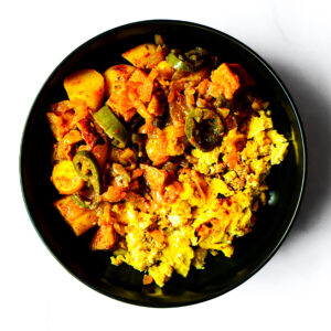 A black bowl filled with a mixed vegetable curry and a yellow rice dish, photographed from above on a white background.