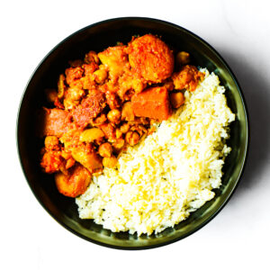 A bowl containing white rice and a chickpea and vegetable stew with chunks of carrots and potatoes on a white background.