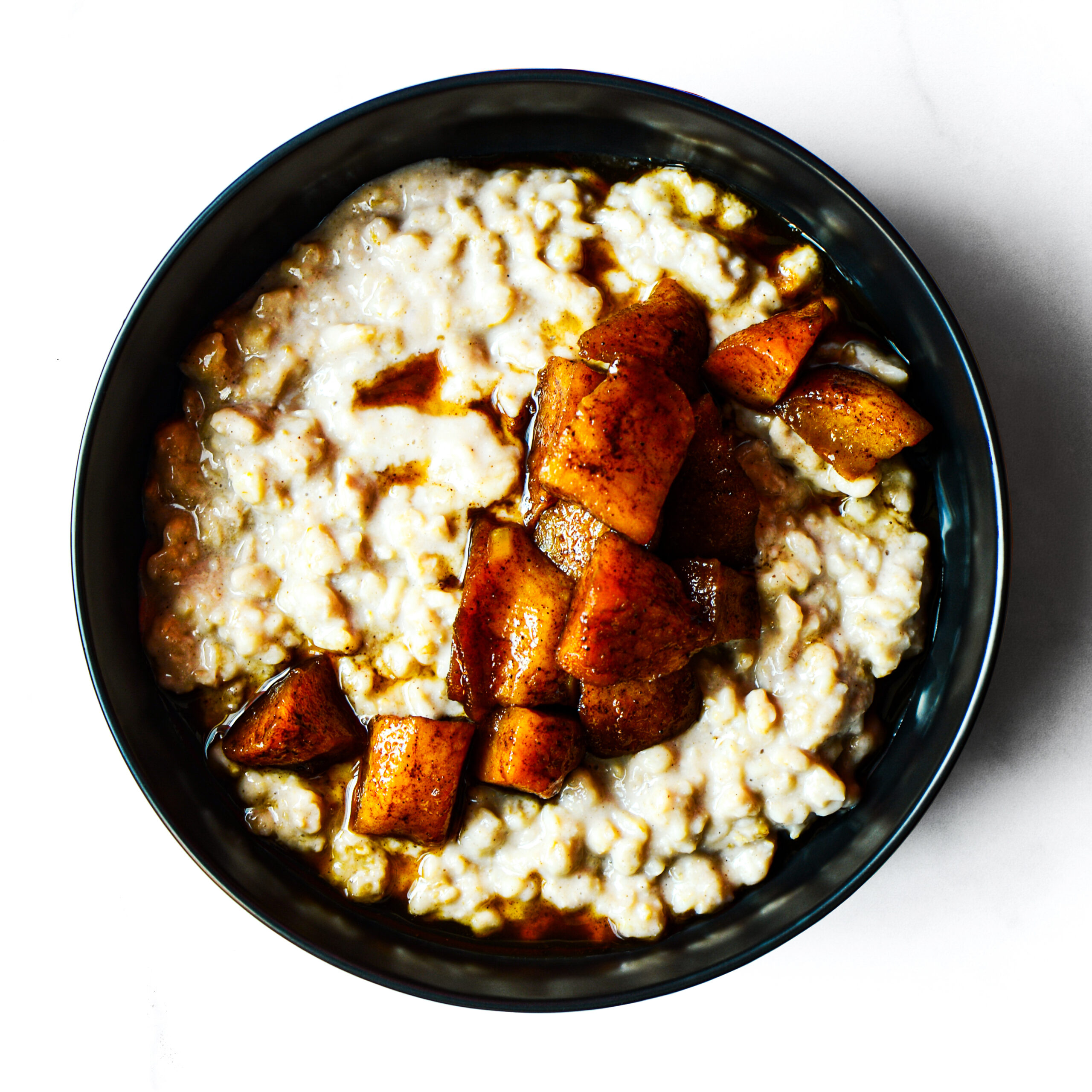 A bowl of oatmeal topped with caramelized, cinnamon-spiced apple chunks on a white background.